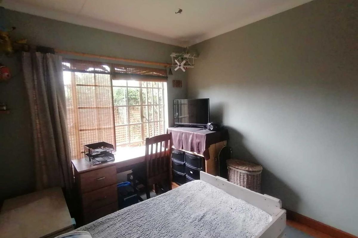 A bedroom featuring a large window with security bars, providing natural light and a view of the exterior area.