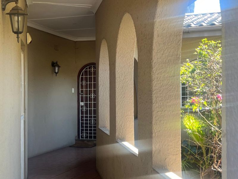 A covered patio area featuring arched masonry columns, tiled flooring, and a secure entrance gate, providing a sheltered outdoor transition space.