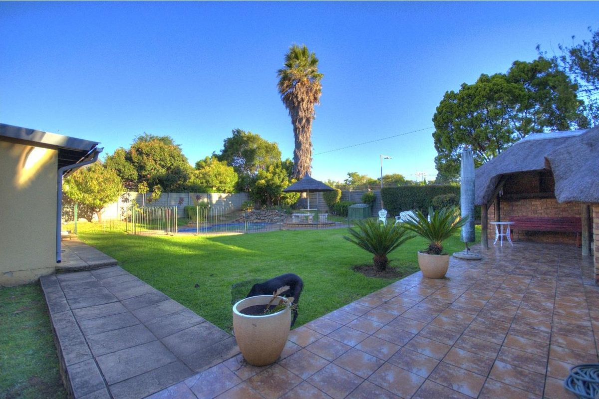 Spacious rear garden featuring a tiled patio, swimming pool with safety fencing, and a traditional thatched lapa area for outdoor entertaining.