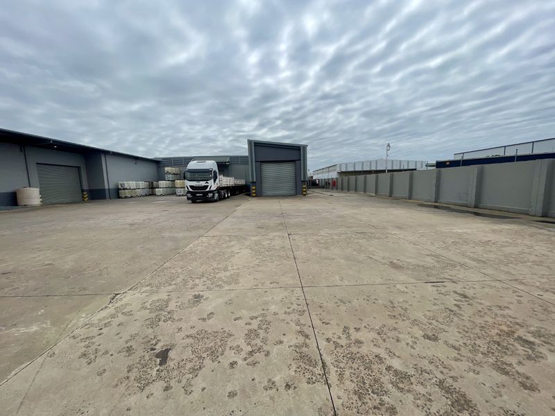 Spacious industrial concrete yard featuring multiple roller shutter doors and secure perimeter walling, suitable for heavy vehicle access and logistics operations.