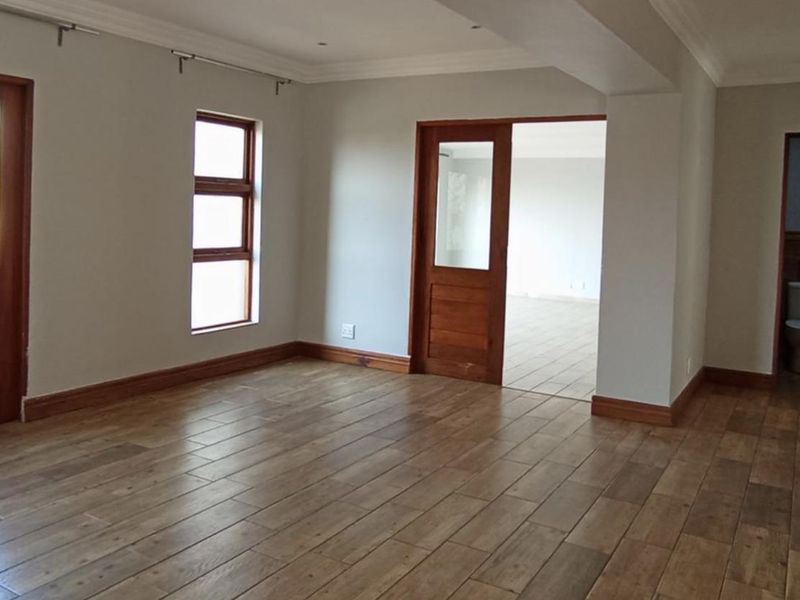 Spacious living area featuring timber-look floor tiles, neutral walls, and classic wooden door frames, offering a clean and versatile space.