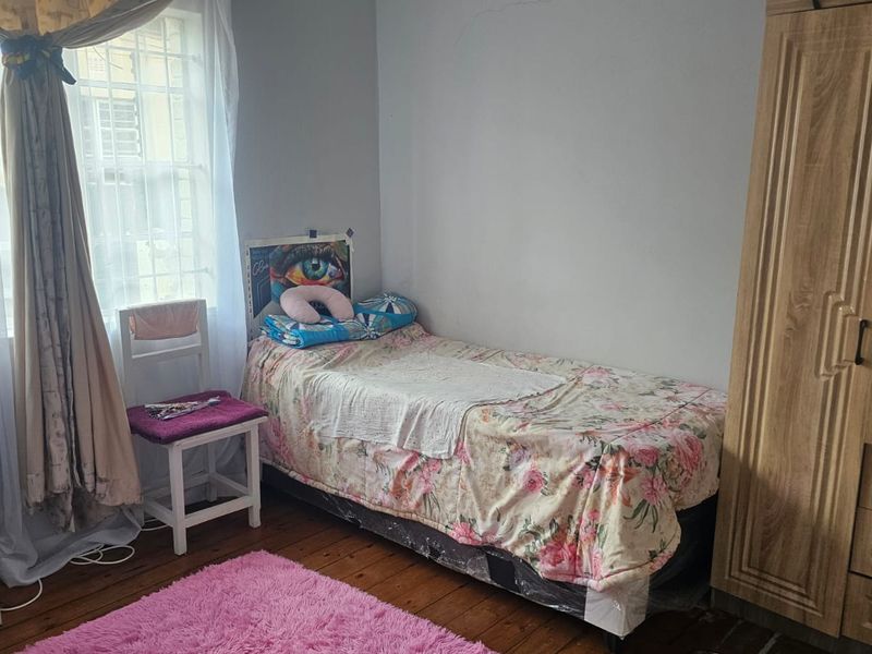 A bedroom featuring timber flooring and a window with security bars, showing signs of wear including visible wall cracks.