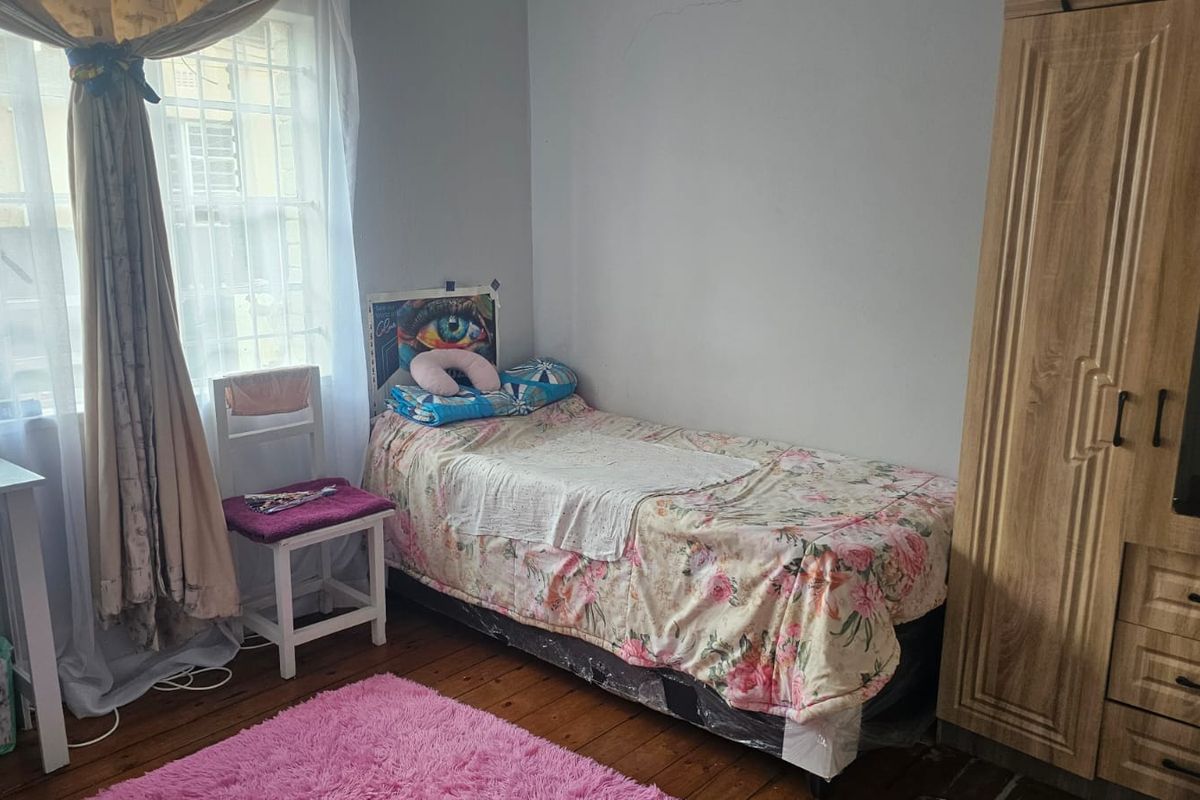 A bedroom featuring timber flooring and a window with security bars, showing signs of wear including visible wall cracks.