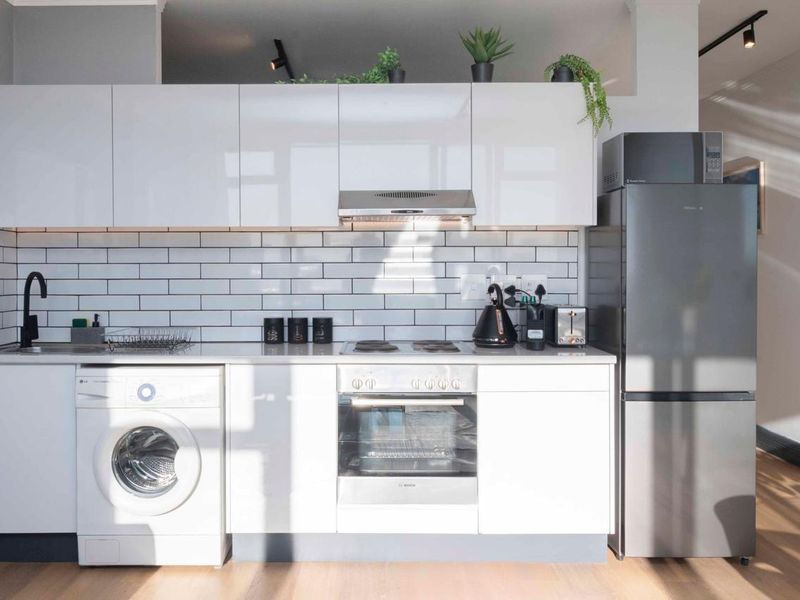 Modern kitchen featuring white gloss cabinetry, subway tile backsplash, integrated appliances, and sleek track lighting in a clean, contemporary design.
