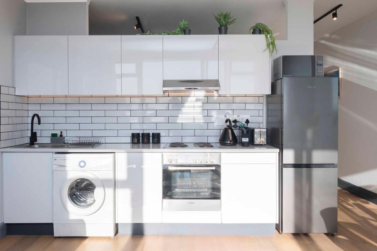 Modern kitchen featuring white gloss cabinetry, subway tile backsplash, integrated appliances, and sleek track lighting in a clean, contemporary design.