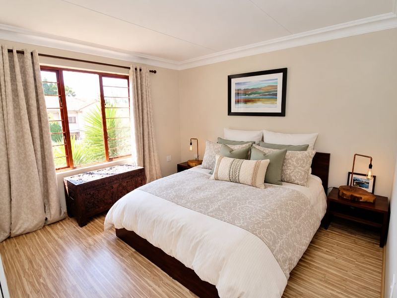 A well-maintained bedroom featuring light-toned laminate flooring, neutral wall finishes, and a large window allowing for natural light.