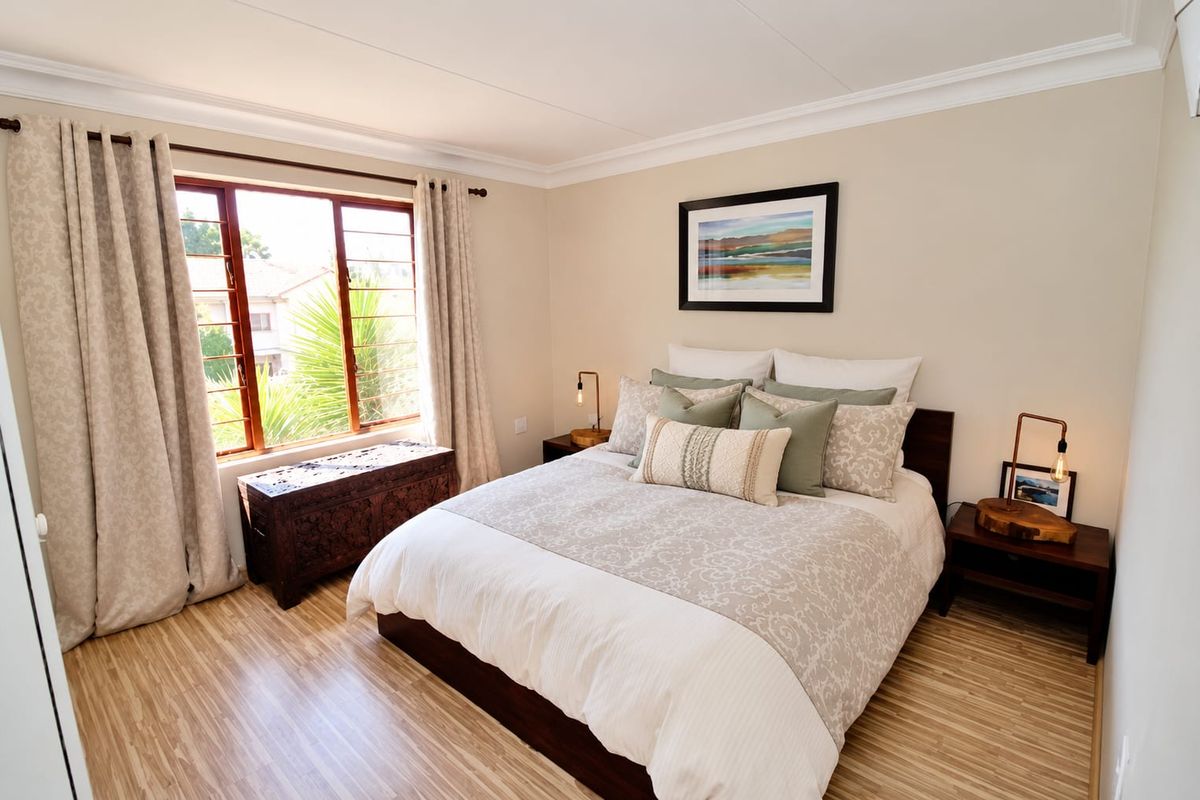 A well-maintained bedroom featuring light-toned laminate flooring, neutral wall finishes, and a large window allowing for natural light.