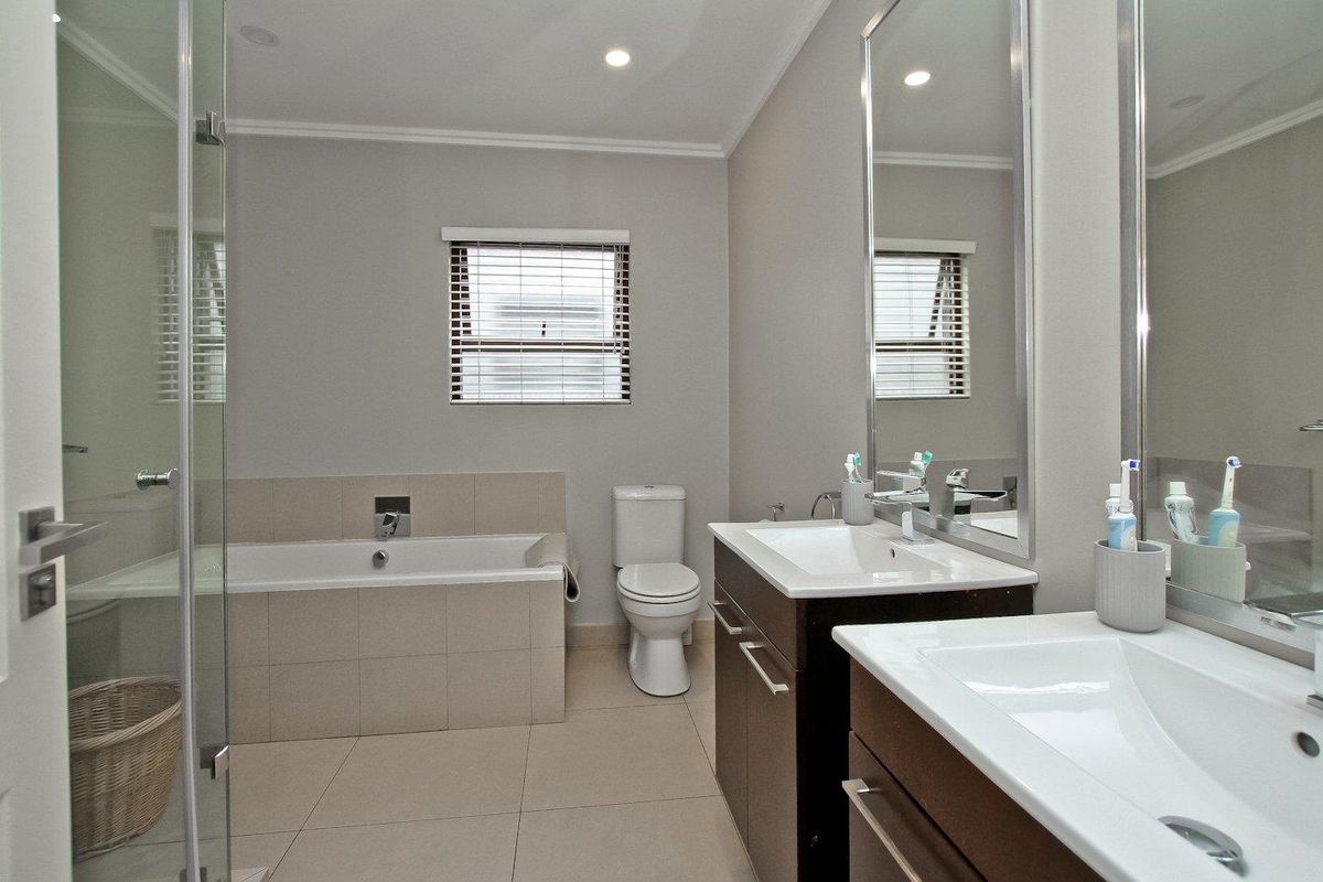 Modern bathroom featuring a double vanity, built-in bathtub, glass-enclosed shower, and neutral tile finishes.
