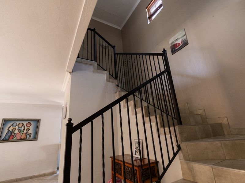 A bright hallway featuring a staircase with a decorative wrought iron balustrade and tiled steps, leading to an upper level.
