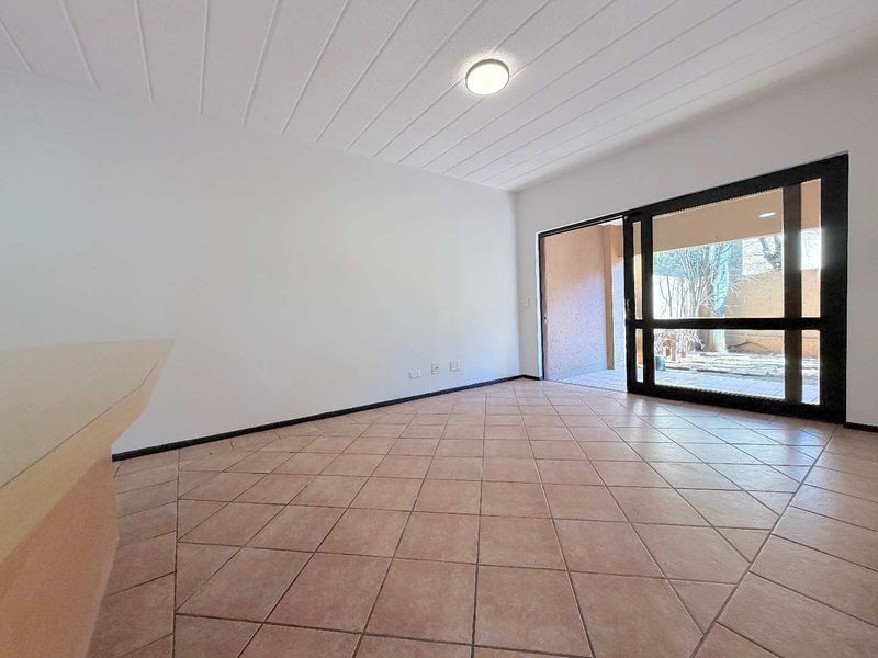 An empty living room featuring tiled flooring, a textured ceiling, and a large sliding glass door providing access to an outdoor patio area.