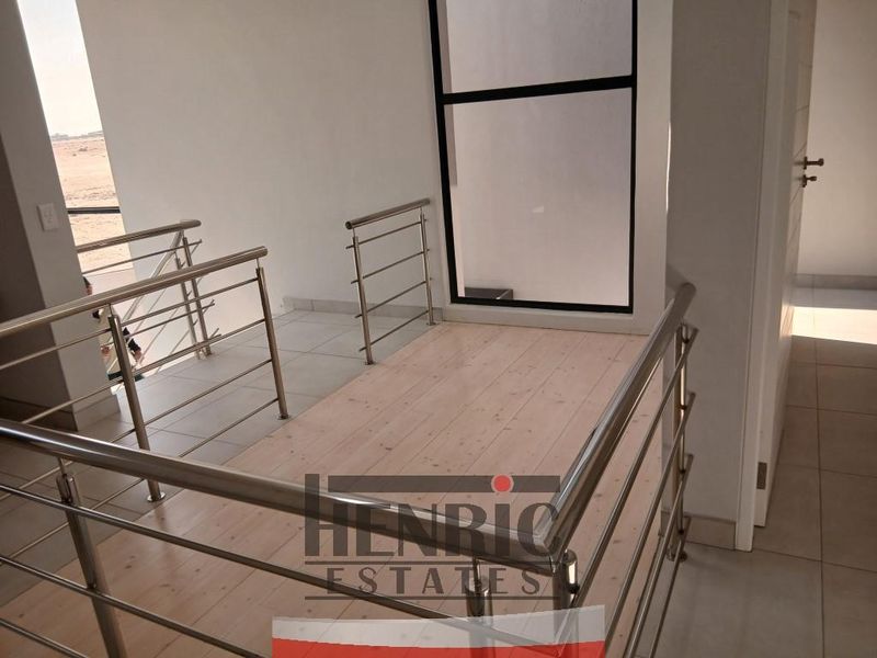A bright, modern landing or hallway area featuring stainless steel balustrades, tiled and timber-look flooring, and large windows providing natural light.
