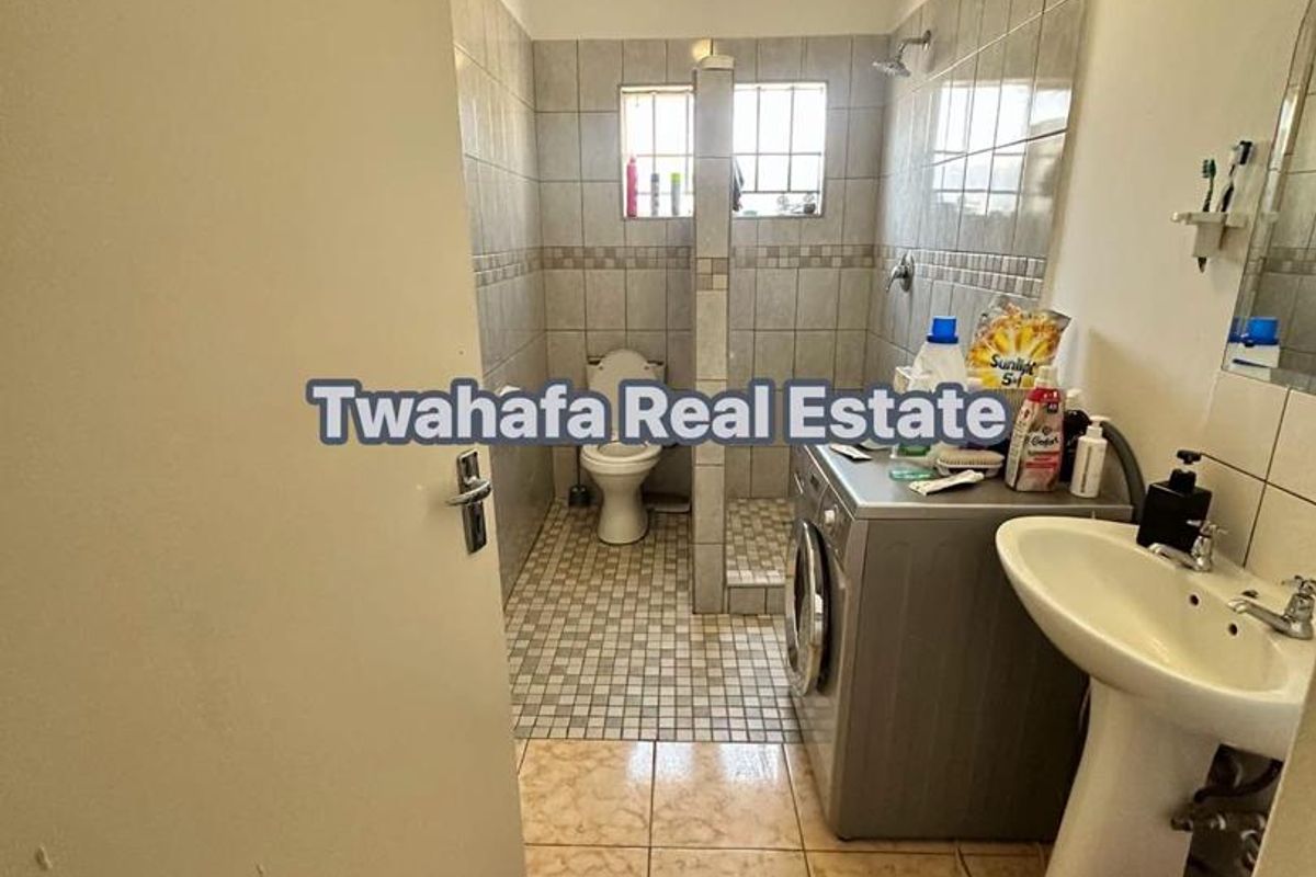 A functional bathroom featuring a pedestal washbasin, toilet, and a tiled shower enclosure with integrated laundry space.