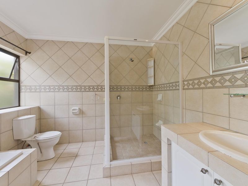 A functional bathroom featuring a tiled shower enclosure, built-in vanity with basin, and toilet, finished with neutral wall and floor tiles.