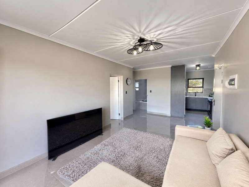 A bright open-plan living area featuring polished tiled floors, a modern ceiling light, and a view through to a contemporary kitchen.