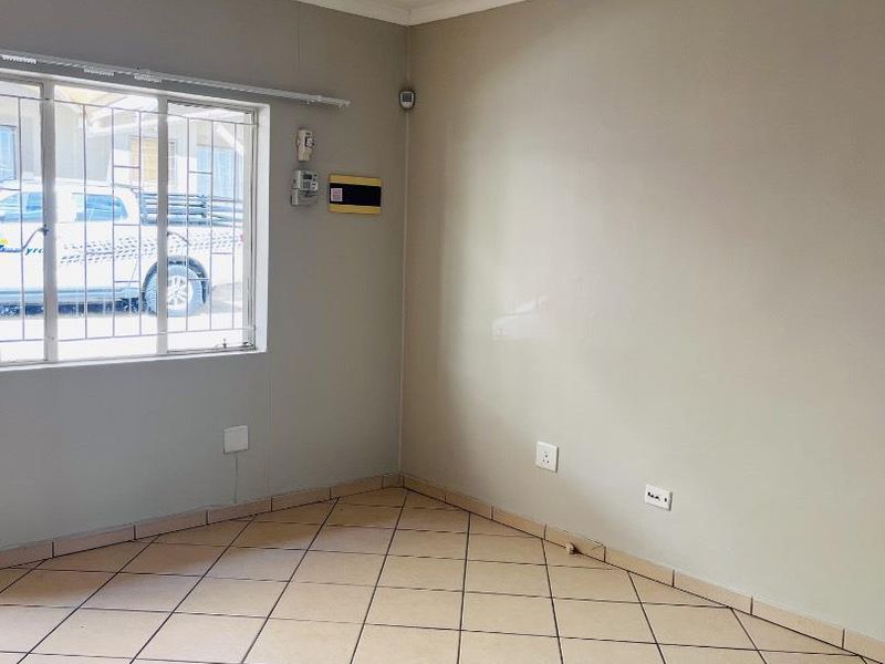 An empty living room featuring neutral wall paint, ceramic tiled flooring, security bars on the window, and integrated electrical and alarm system fixtures.