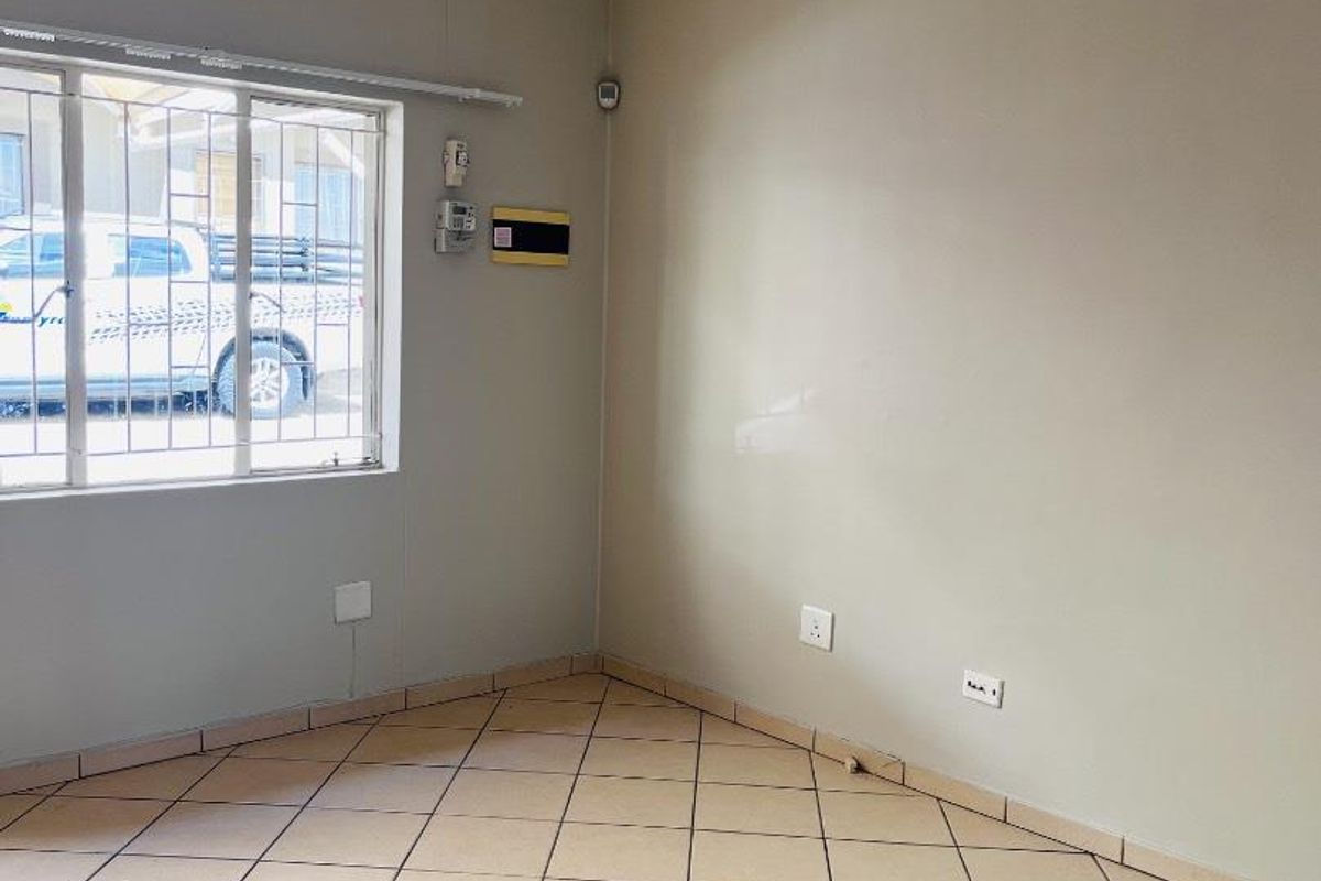 An empty living room featuring neutral wall paint, ceramic tiled flooring, security bars on the window, and integrated electrical and alarm system fixtures.