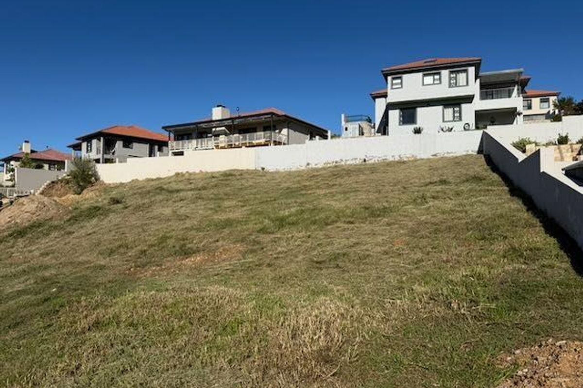 A vacant residential plot featuring a sloping grassy landscape, bordered by retaining walls and situated within an established neighborhood.