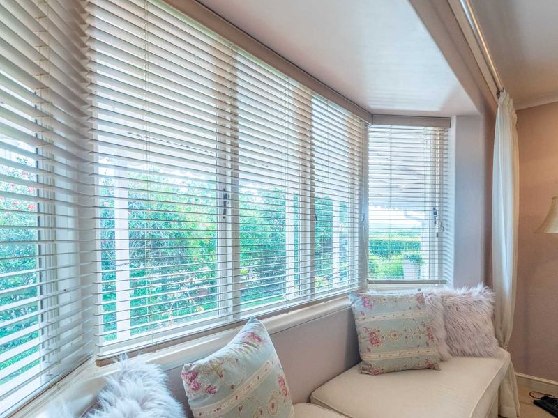 A bright living area featuring a large bay window with fitted horizontal blinds, providing ample natural light and a view of the garden.