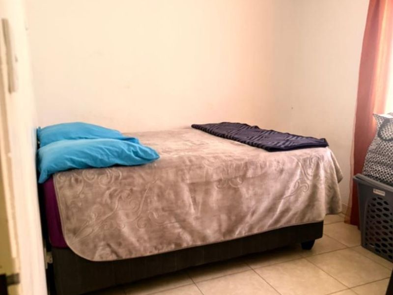 A simple bedroom featuring tiled flooring and neutral wall finishes, providing a functional space for rest.