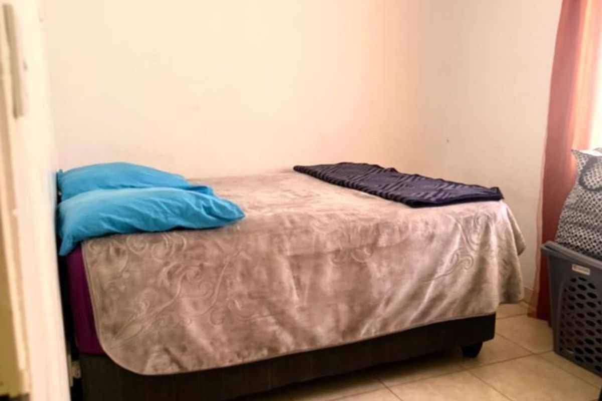A simple bedroom featuring tiled flooring and neutral wall finishes, providing a functional space for rest.