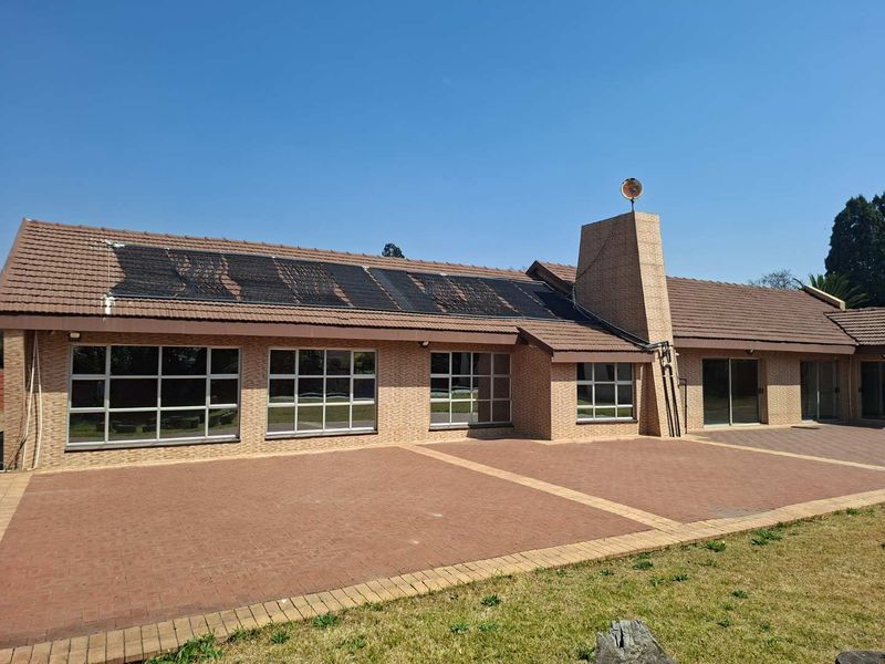 Rear view of the house featuring a large paved patio, brick facade, tiled roof, and integrated solar water heating panels.