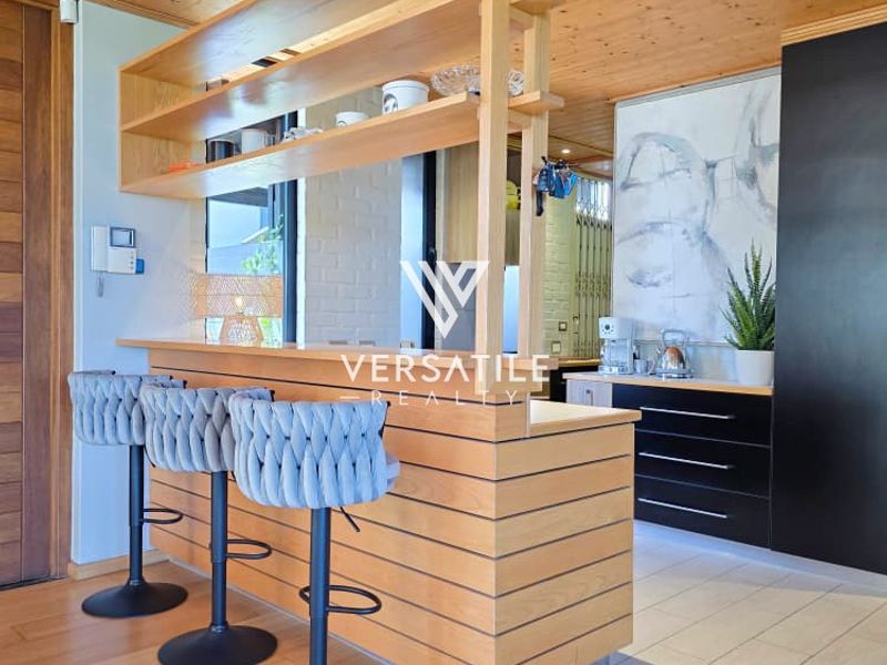 Modern kitchen featuring a timber ceiling, breakfast bar with integrated shelving, and sleek black cabinetry, creating a warm and functional culinary space.