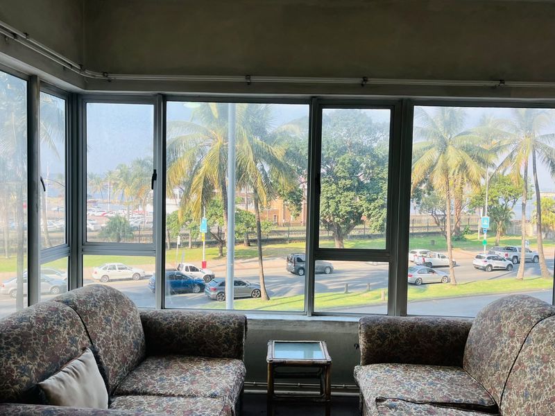 Living area featuring large windows with expansive street and palm tree views, offering significant natural light and potential for modern interior updates.