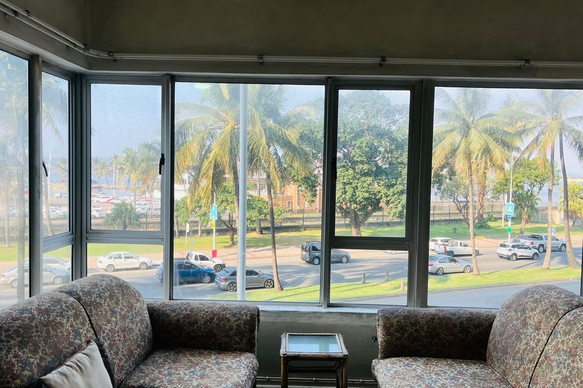 Living area featuring large windows with expansive street and palm tree views, offering significant natural light and potential for modern interior updates.