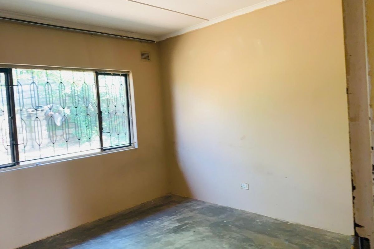 An empty bedroom featuring a sliding window with security bars and an unfinished concrete floor, ready for renovation or flooring installation.