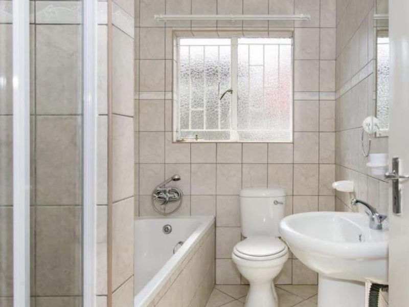 A functional bathroom featuring a bathtub, separate shower enclosure, pedestal basin, and toilet, finished with neutral wall and floor tiles.