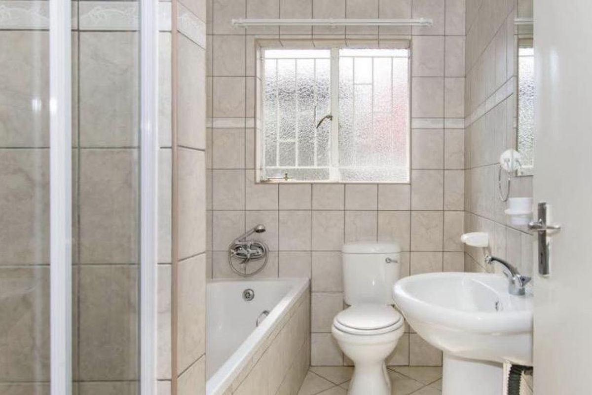 A functional bathroom featuring a bathtub, separate shower enclosure, pedestal basin, and toilet, finished with neutral wall and floor tiles.