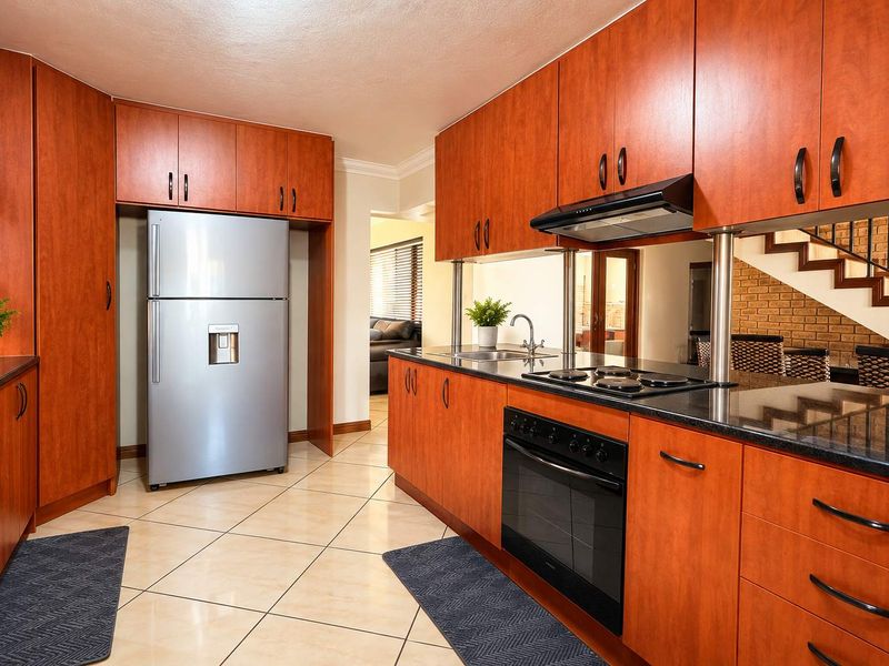 A functional kitchen featuring warm-toned wooden cabinetry, granite countertops, integrated appliances, and a mirrored backsplash, with tiled flooring throughout.