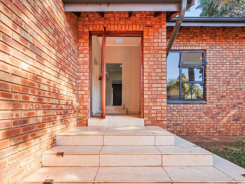 Front entrance of the house featuring a face brick facade, tiled steps leading to the front door, and an aluminium window frame.