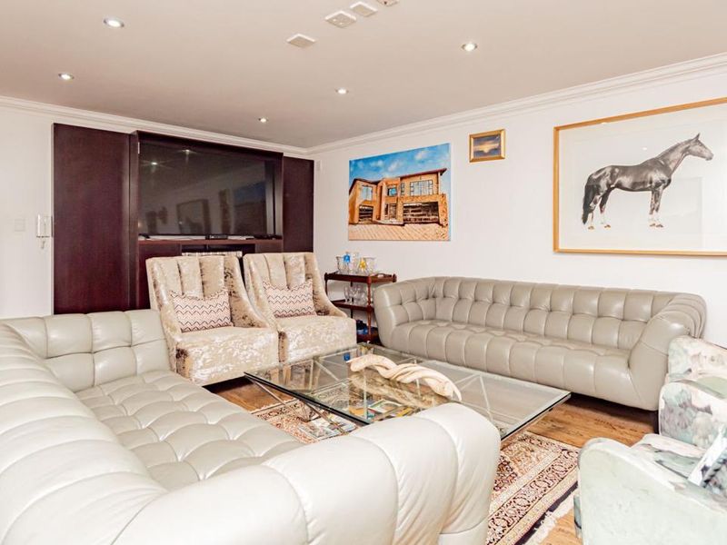 A comfortable living room featuring hardwood flooring, recessed downlighting, crown molding, and custom built-in cabinetry.