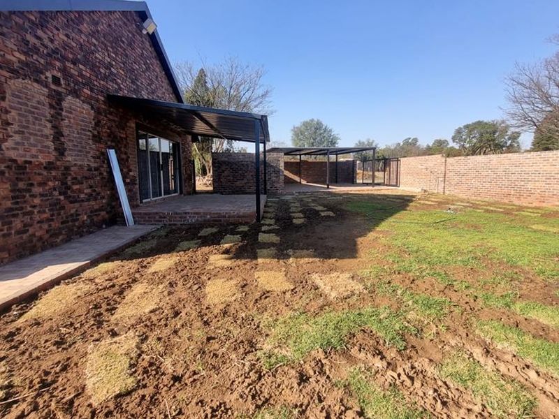 Rear view of the property featuring an exposed brick facade, a covered patio area, and a large garden space currently undergoing landscaping.
