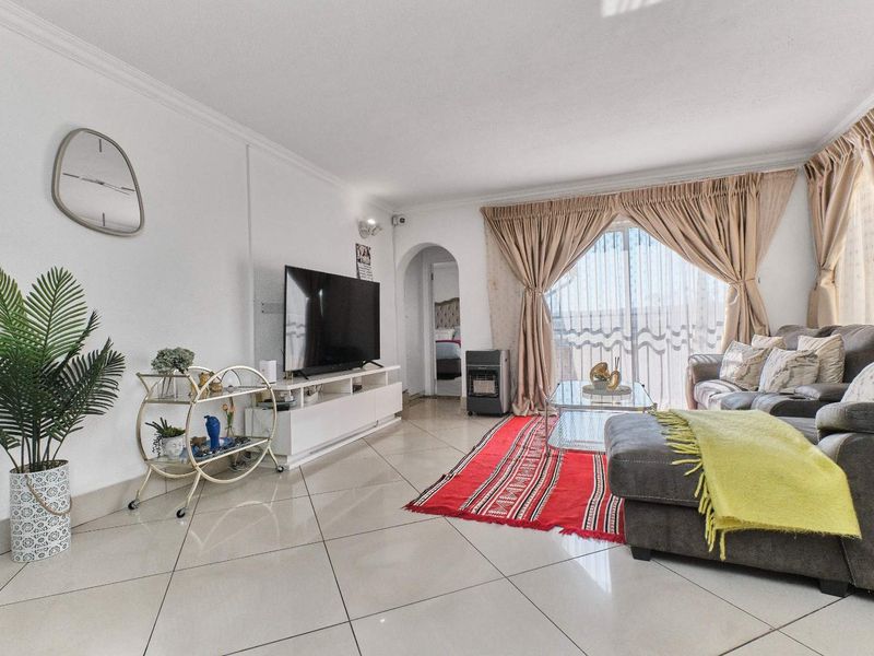 A bright living room featuring polished tiled flooring, an arched entryway, and a large sliding glass door providing access to the exterior.