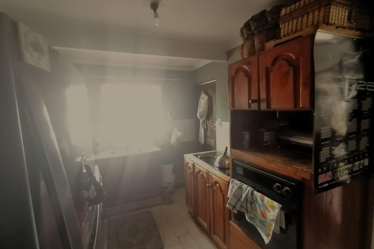 A compact kitchen featuring traditional wooden cabinetry, a built-in oven, and tiled flooring, requiring modernization to improve functionality and aesthetic appeal.
