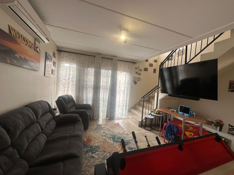 A comfortable living room featuring tiled flooring, a split-system air conditioner, and an integrated staircase with a metal railing leading to the upper level.