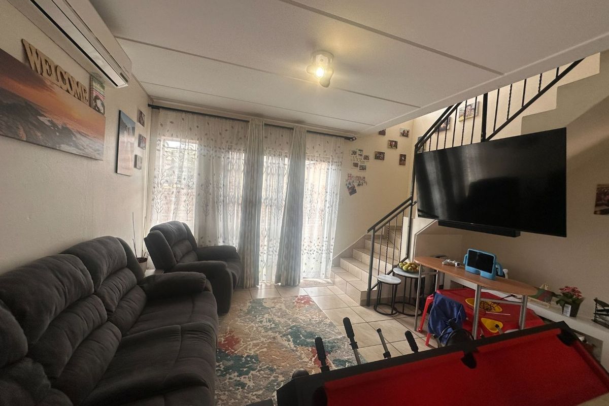 A comfortable living room featuring tiled flooring, a split-system air conditioner, and an integrated staircase with a metal railing leading to the upper level.