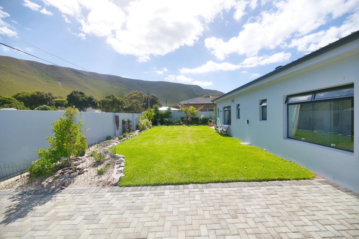 A well-maintained rear garden featuring a paved patio area, manicured lawn, and secure boundary walls with mountain views.
