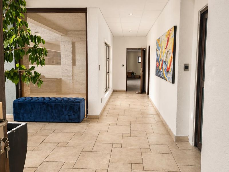 A bright, spacious hallway featuring neutral tiled flooring, recessed ceiling lights, and access to multiple rooms through timber-framed doorways.