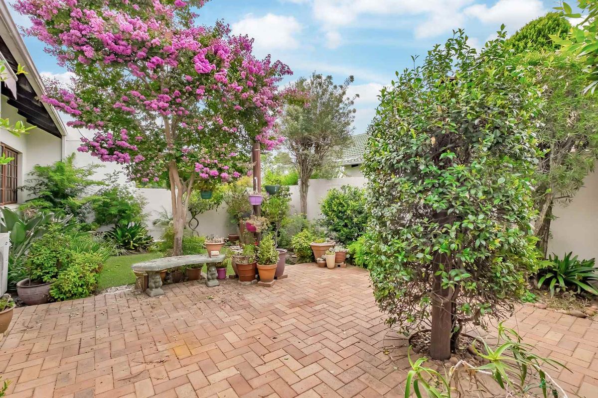 A private rear garden featuring a brick-paved patio area, established trees, and perimeter boundary walls.