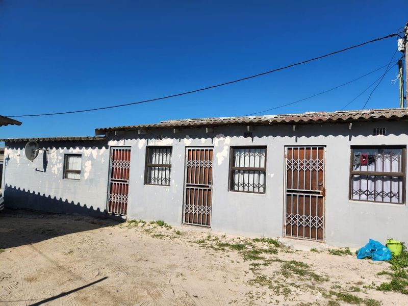 Rear exterior view of a single-story residential building featuring security gates and bars on windows, showing signs of weathered paint and exterior wear.