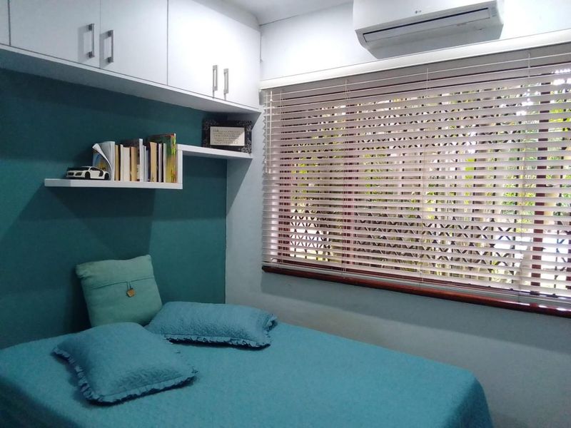 A compact bedroom featuring built-in overhead storage, wall-mounted shelving, and a split-system air conditioning unit, finished with venetian blinds.