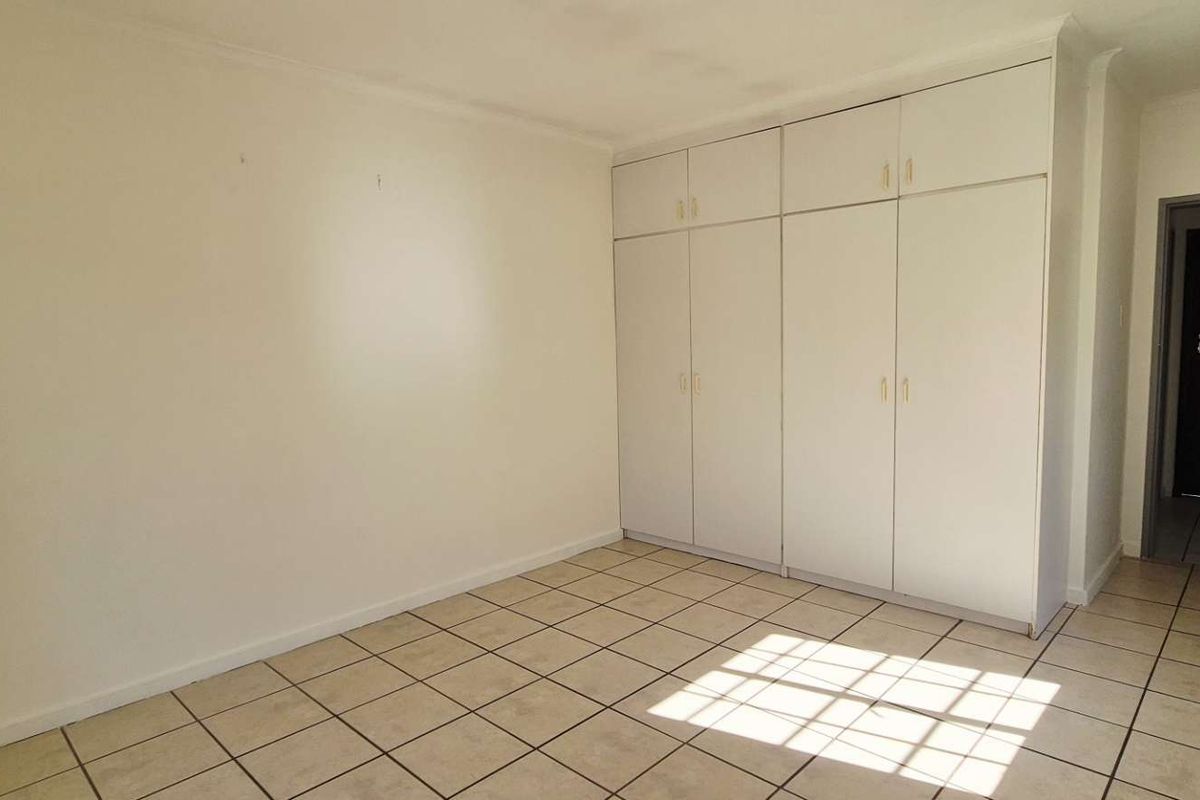 A bright, empty bedroom featuring neutral tiled flooring and floor-to-ceiling built-in cupboards, offering a clean and versatile space.
