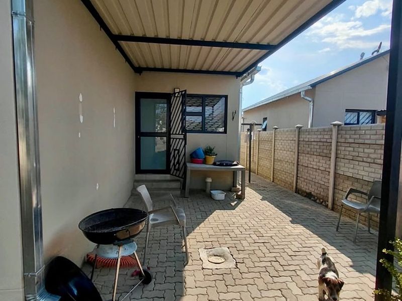 A covered outdoor patio area featuring paved flooring and a brick boundary wall, providing a functional space for outdoor living.