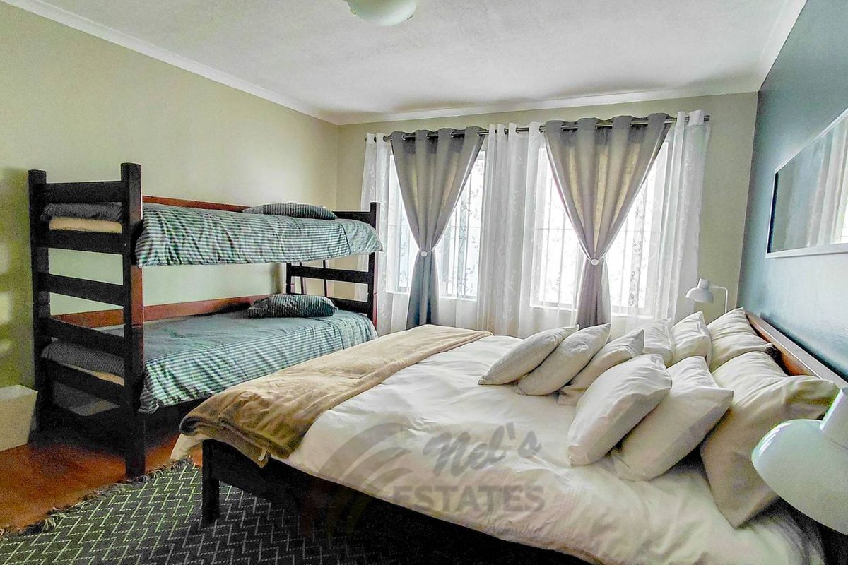 A spacious bedroom featuring large windows with curtains, providing ample natural light and a functional layout suitable for multiple occupants.