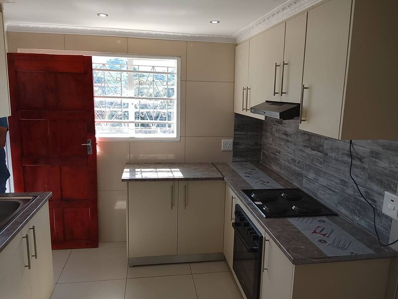 Modern kitchen featuring sleek cabinetry, laminate countertops, built-in oven, electric hob, and an extractor fan, with tiled flooring and a secure exterior door.
