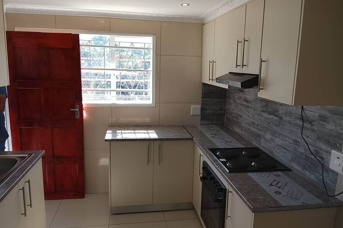 Modern kitchen featuring sleek cabinetry, laminate countertops, built-in oven, electric hob, and an extractor fan, with tiled flooring and a secure exterior door.