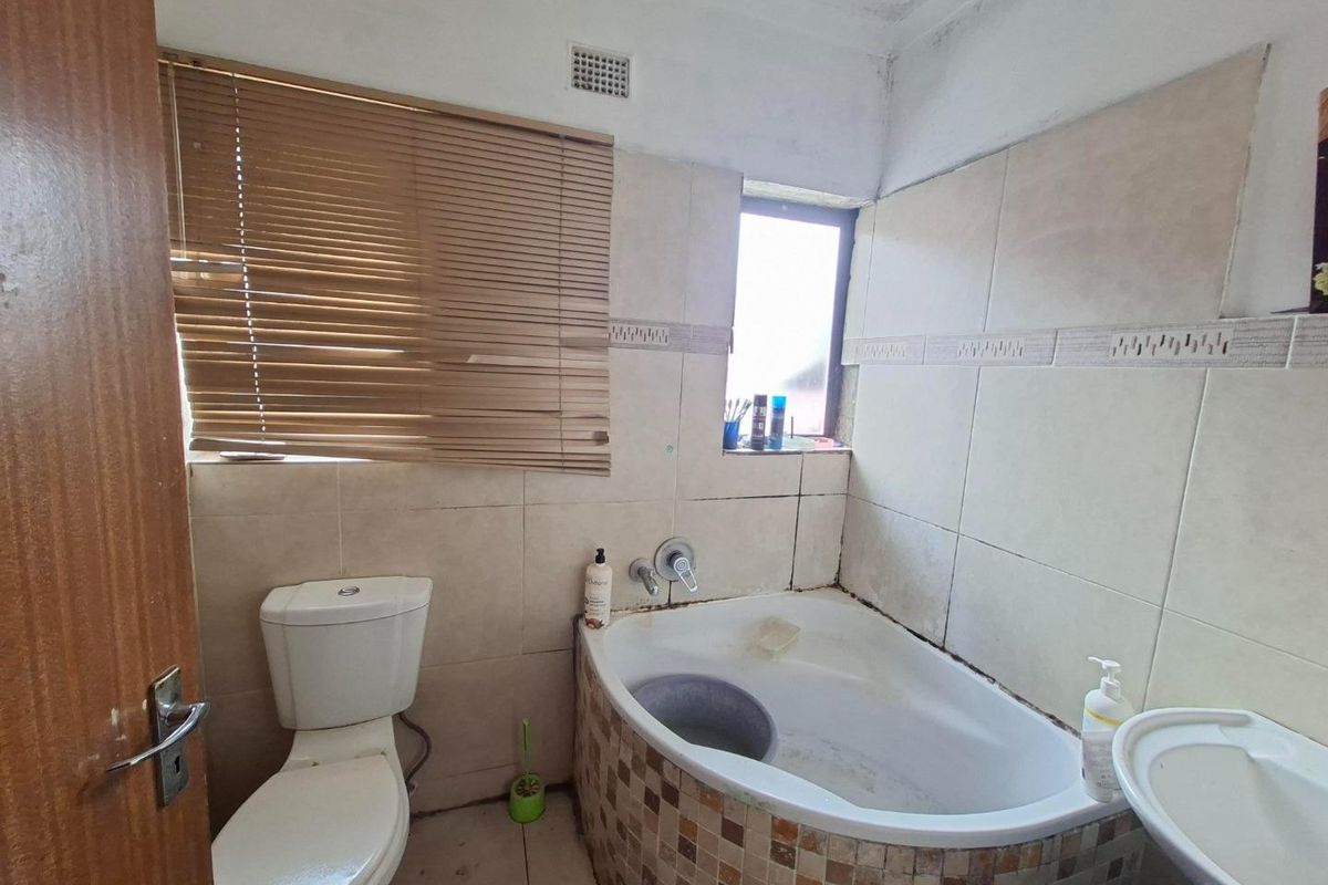 A compact bathroom featuring a corner bathtub, toilet, and basin with tiled finishes. The space requires cosmetic updates and maintenance to improve its condition.